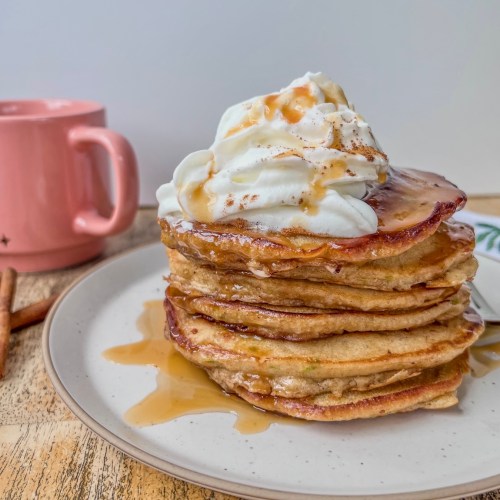 Caramel apple pancakes with whipped cream, caramel drizzle, and cinnamon on top.