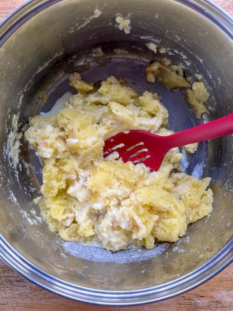 Yellow potatoes mashed in a pot with some freshly added heavy cream.