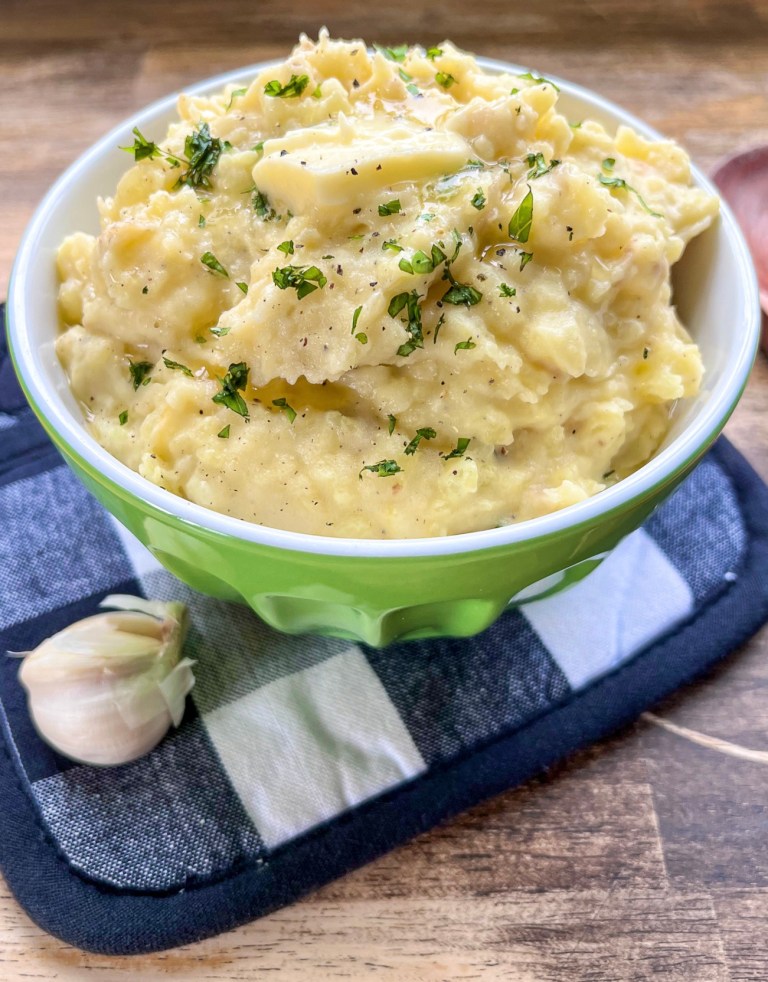 Creamy garlic mashed potatoes in a large bowl with some butter and fresh basil on top.