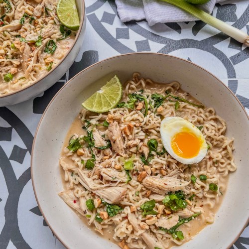 Easy sweet and spicy chicken ramen with fresh herbs, lime wedges, and soft-boiled eggs on top.