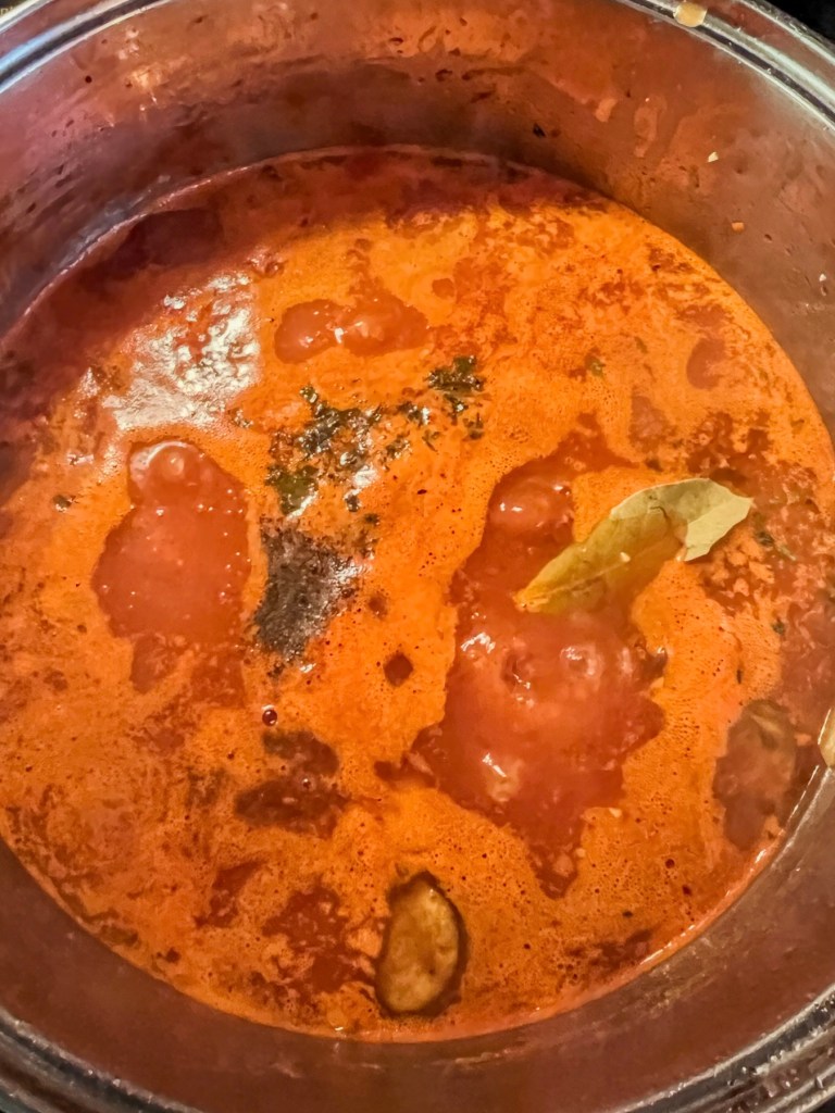 A large pot filled with veggies, spices, herbs, and broth cooking on the stove.