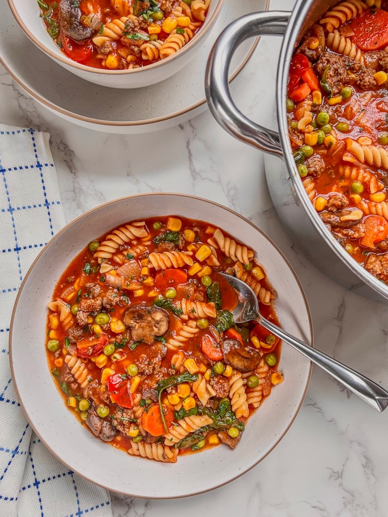 Rotini and beef vegetable soup dished into bowls with a large pot filled with more off to the side.
