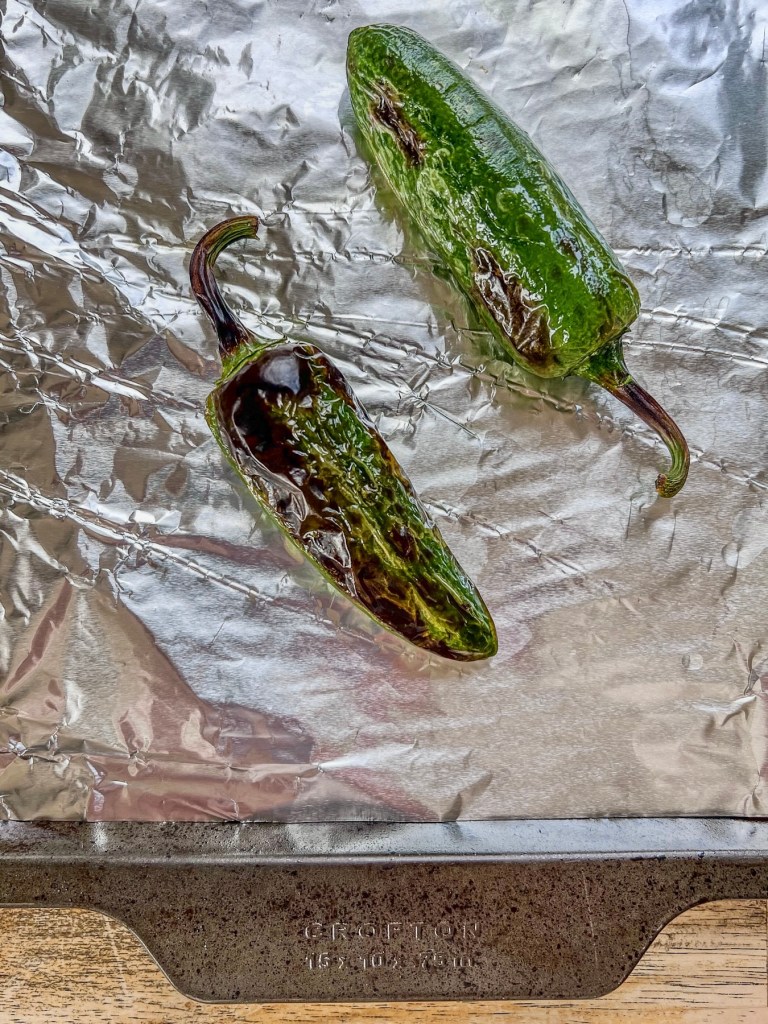 Charred and blistered jalapeños on a baking sheet lined with foil.