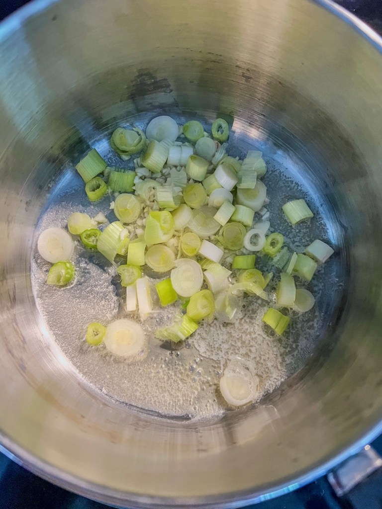 Butter, garlic, and green onions cooking in a saucepan.