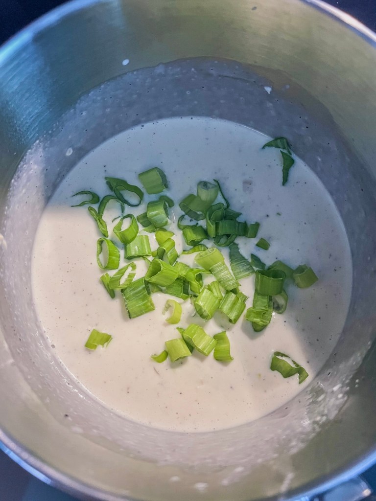 White cheddar sauce coming together in a saucepan with some newly added green onions.