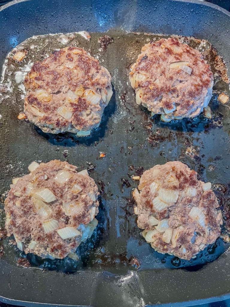 Onion jalapeño burgers cooking in a grill pan on the stove.