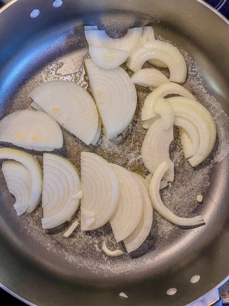Onions cooking in a skillet on the stove until they caramelize.