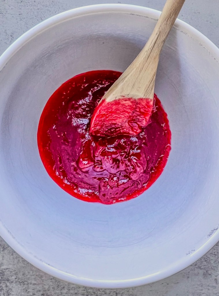 Cranberry compote in a mixing bowl with a wooden spoon inside.