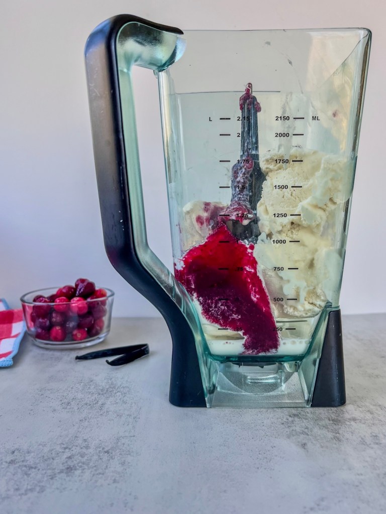All of the ingredients for a cranberry vanilla bean milkshake in a large blender, just before blending.