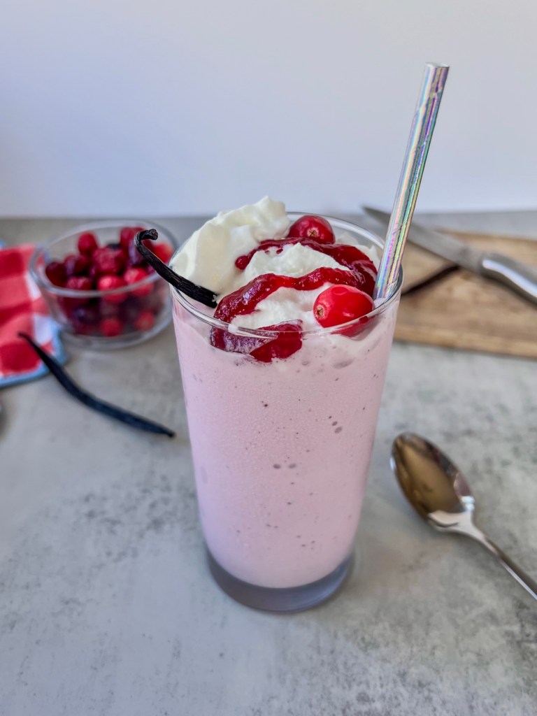 Cranberry vanilla bean milkshake with whipped cream, cranberry compote, and a vanilla bean on top.