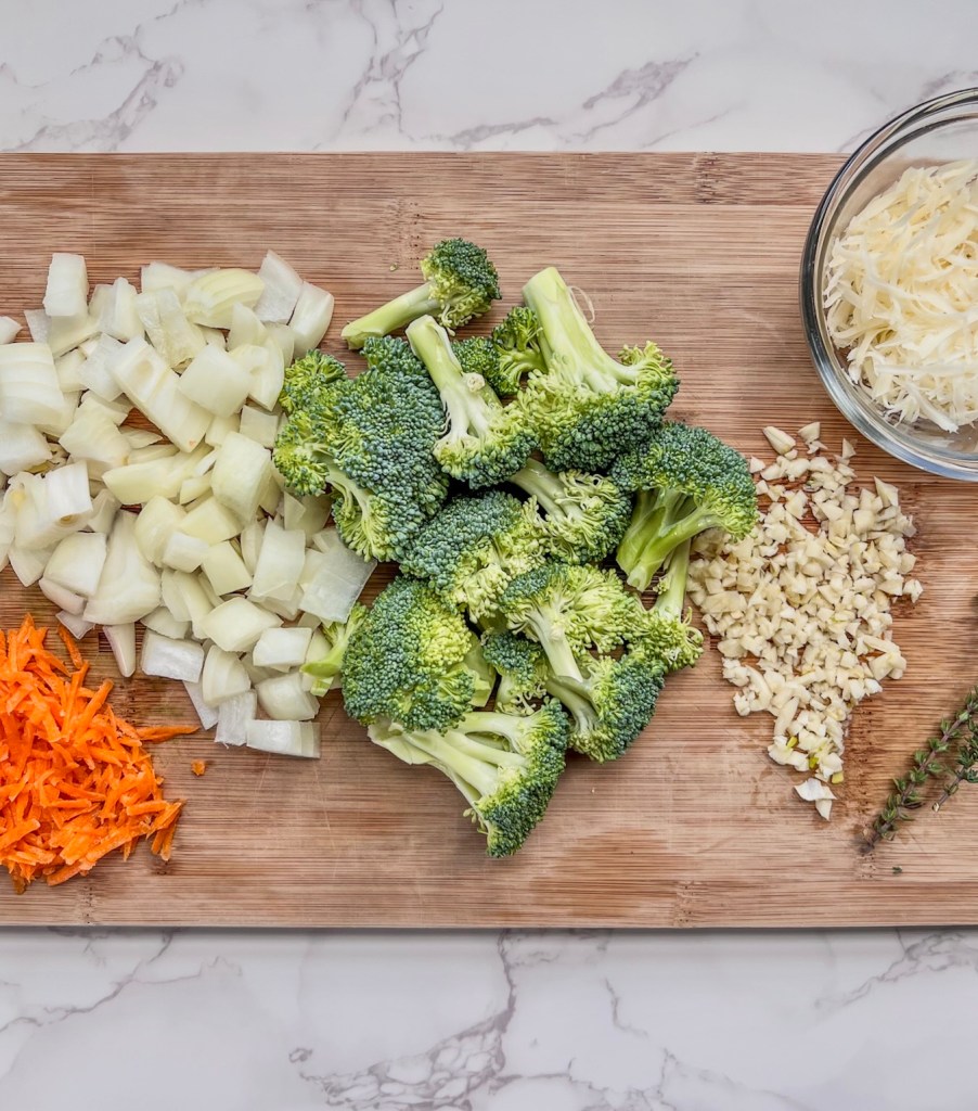 Carrots, onion, broccoli, garlic, and parmesan cheese prepped on a wooden cutting board