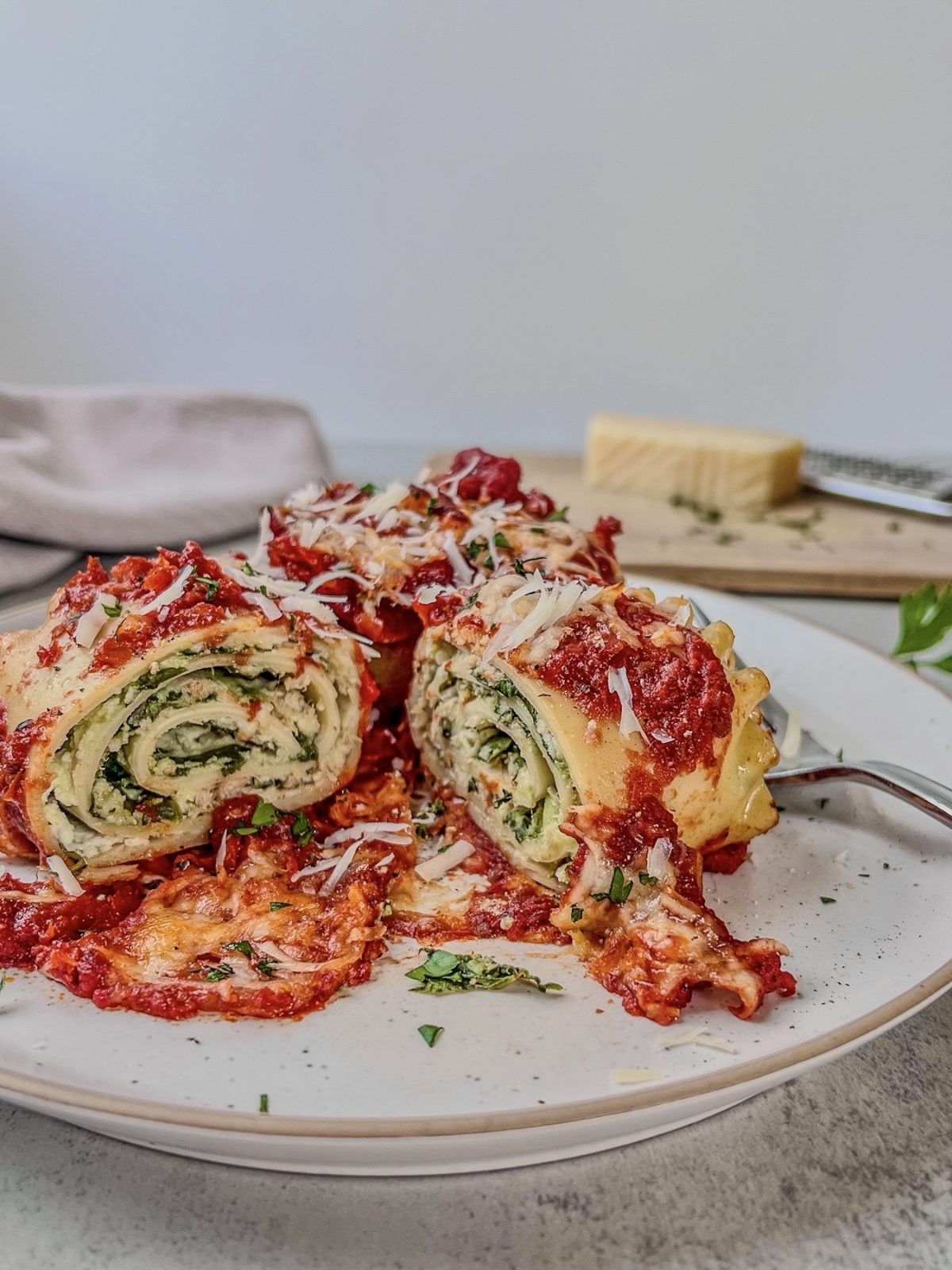 Creamy spinach lasagna roll ups with tuna served with fresh herbs and parmesan cheese on top.
