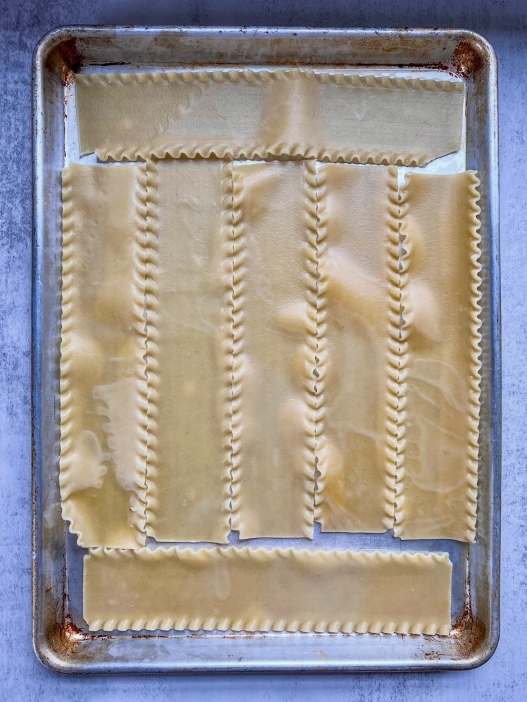 Cooked lasagna noodles spread out on an oiled baking sheet.