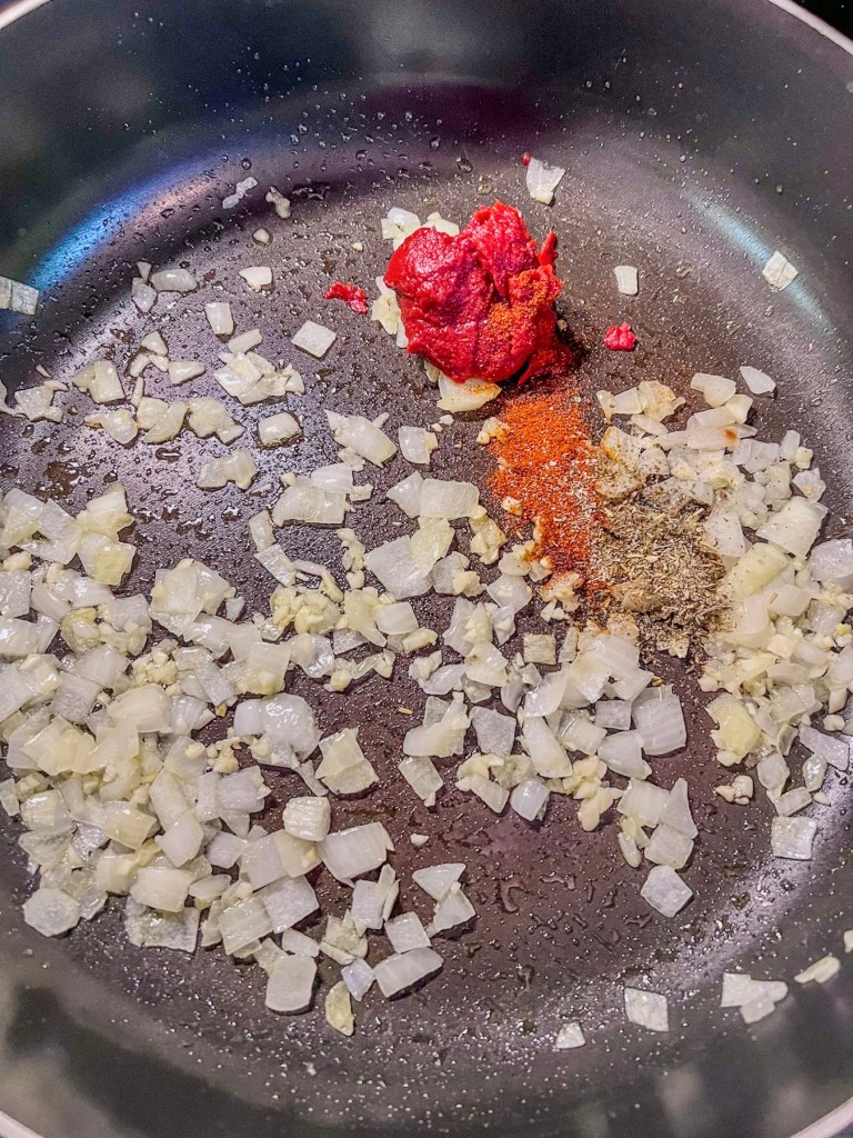 Onions, garlic, spices, and tomato paste cooking in a skillet to make a sauce.