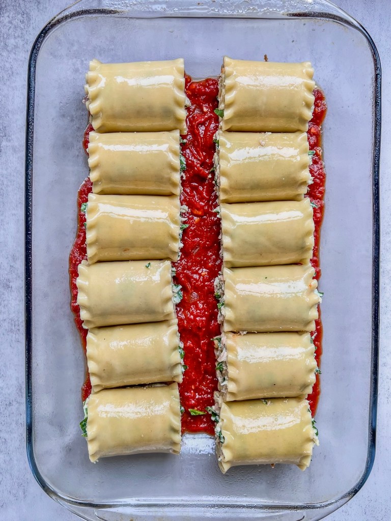 Creamy spinach lasagna roll ups with tuna in a baking pan nestled in some fresh marinara sauce.
