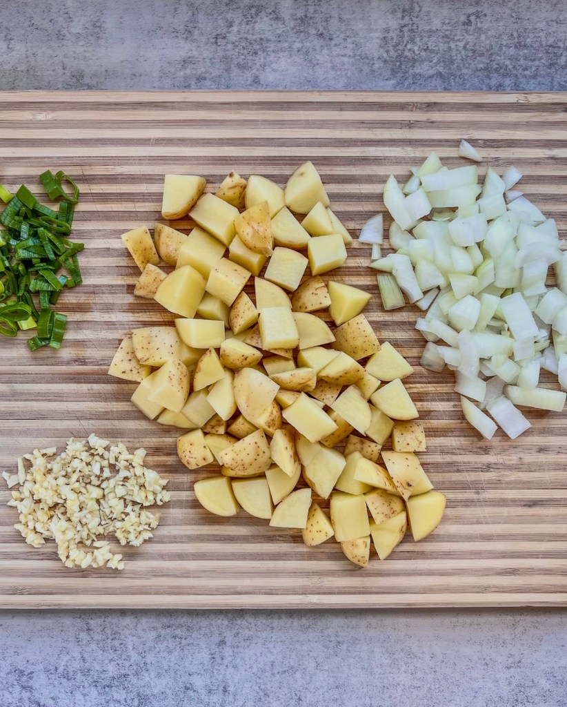 Potatoes, onion, garlic, and jalapeno prepped on a cutting board.