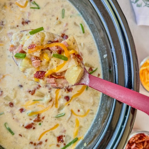 Crockpot loaded ham and potato soup with shredded cheese, bacon, and green onion garnished on top.