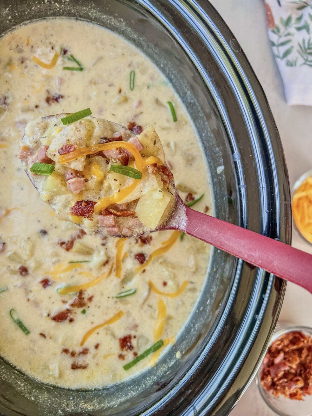 Crockpot loaded ham and potato soup with shredded cheese, bacon, and green onion garnished on top.