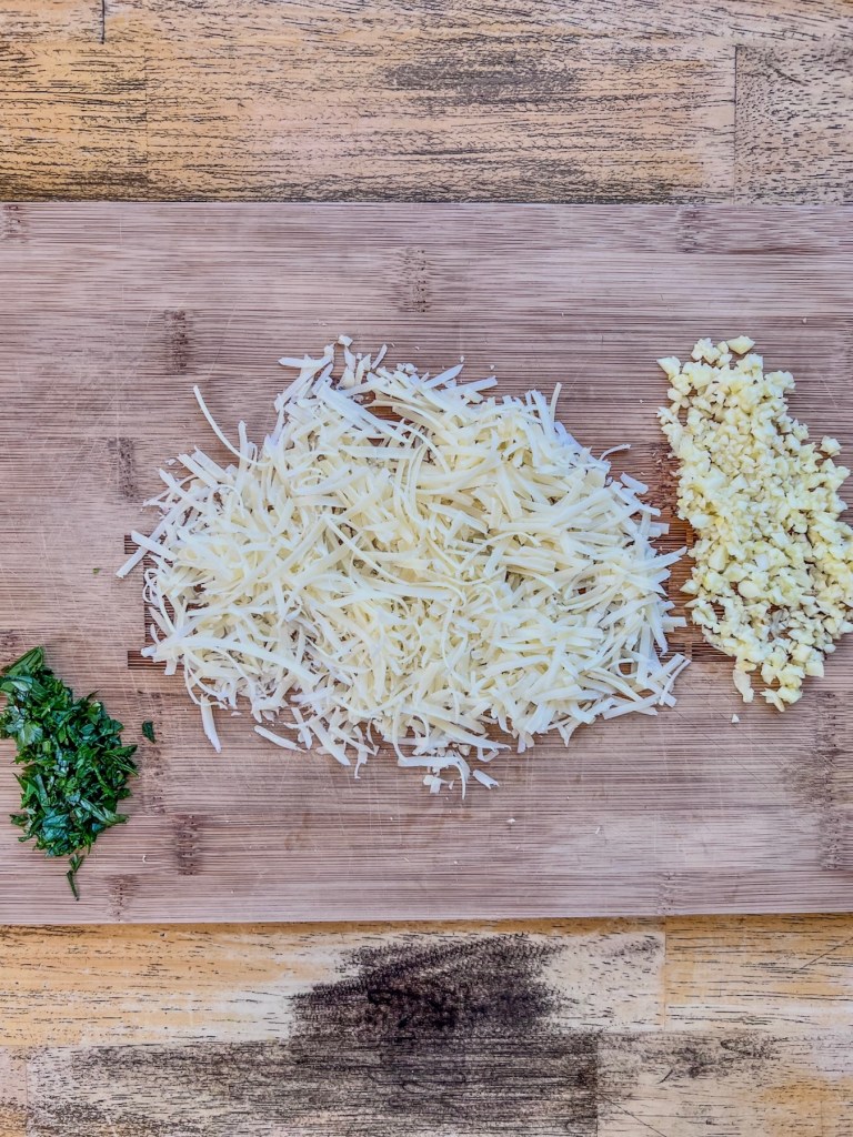 Parmesan, parsley, and garlic prepped on a cutting board.