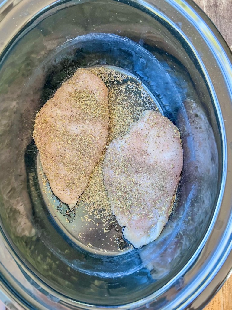 Chicken breasts in a crockpot with some seasonings sprinkled on top.