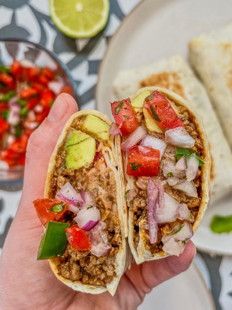 Loaded beef burritos on a plate with one sliced in half to show the middle